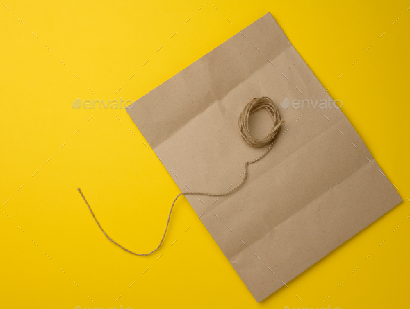 Blank brown kraft paper bag and jute rope on yellow background