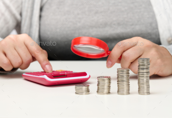 Woman sits at a table and counts on a calculator in the other hand a magnifying glass