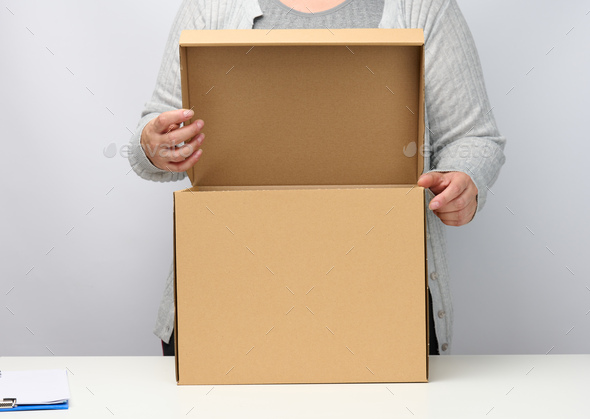 Woman in gray clothes stands and holds open brown box on a white background