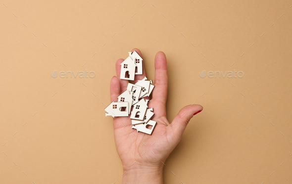 Woman\'s hand holds miniature wooden houses. Real estate search concept