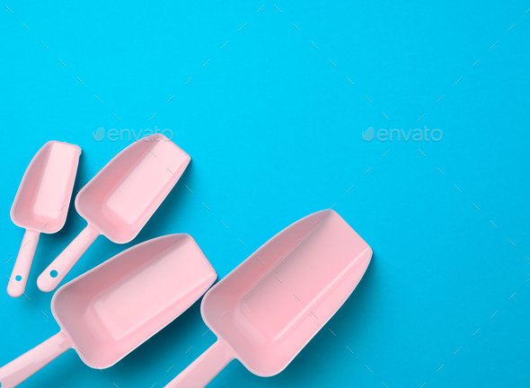 Set of pink plastic kitchen scoops for bulk products on a blue background, flat lay