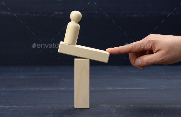 Wooden figure of a man stands on a swing, his finger keeps balance. Concept of help