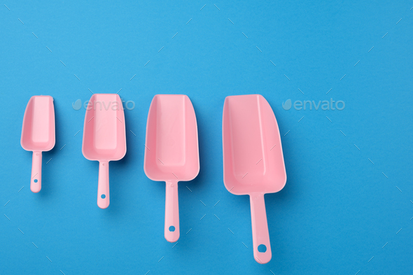 Set of pink plastic kitchen scoops for bulk products on a blue background