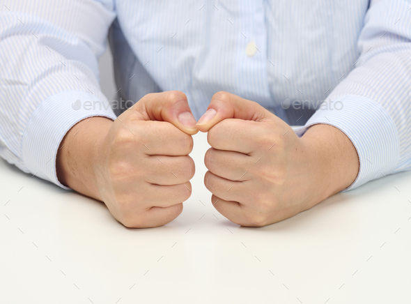 Two female hands folded into a fist on a white table. Strict leader