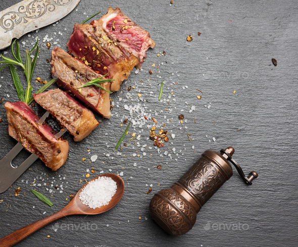 Sliced fried beef steak New York on a black background with spices, degree of doneness rare