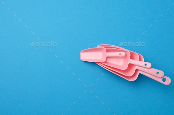 Set of pink plastic kitchen scoops for bulk products on a blue background