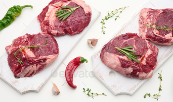 Raw piece of beef ribeye with rosemary, thyme on a white table