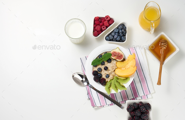Milk, plate with oatmeal porridge and fruit, freshly squeezed juice in a transparent glass decanter