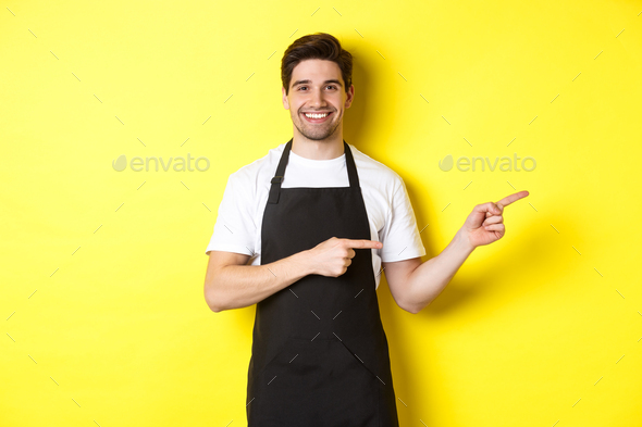 Friendly waiter pointing fingers right, showing your logo or promo offer, wearing black apron