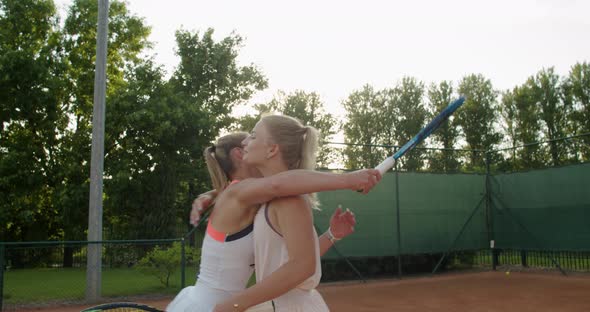 Two Happy Women Players Hugging After Tennis Match Standing on Clay Court