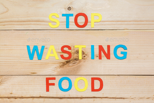 Stop wasting food. The inscription of letters cut out of color cardboard on a wooden background