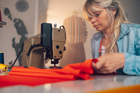 Tailor woman sitting and sewing on a sewing machine a in studio