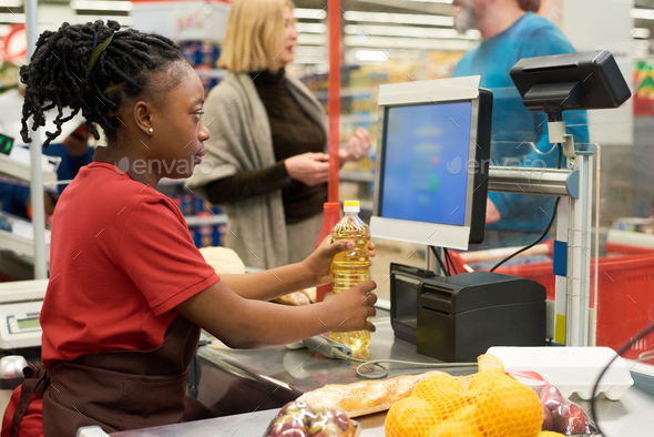 Saleswoman checking price of sunflower oil while holding it over cashier counter
