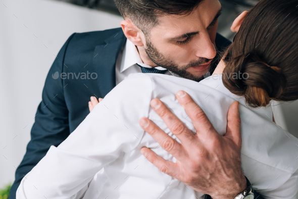 cropped view of businessman hugging and kissing secretary in office