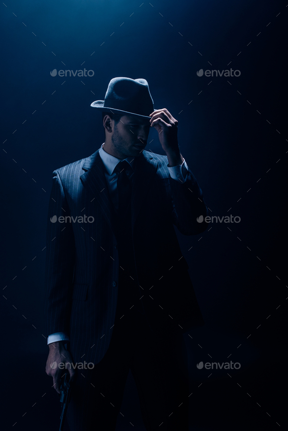 Gangster touching felt hat and holding gun on dark background Stock ...