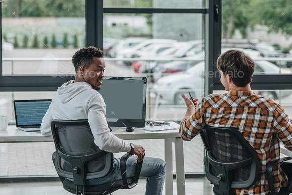 back view of young programmer talking to african american colleague in office