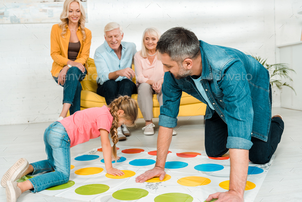 KYIV, UKRAINE - NOVEMBER 21, 2019: cheerful father and daughter playing twister game near family