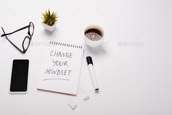 notebook with change your mindset inscription near felt-tip pen, coffee cup, potted plant, glasses,
