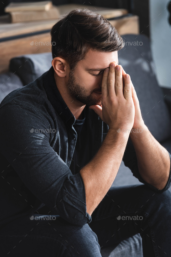 sad man with closed eyes obscuring face in apartment