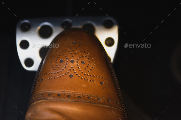 partial view of male leg in elegant brown shoe on car brakes pedal