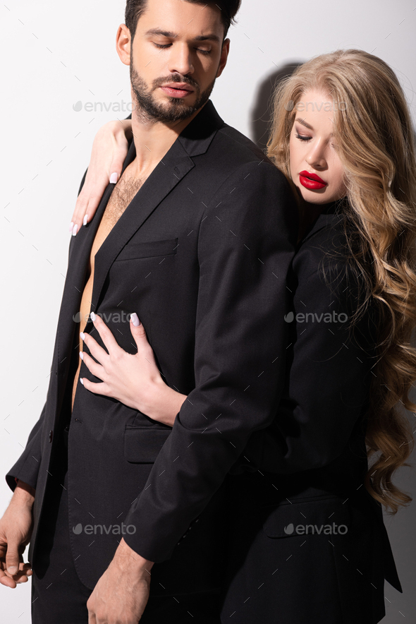 attractive young woman hugging muscular man in suit on white