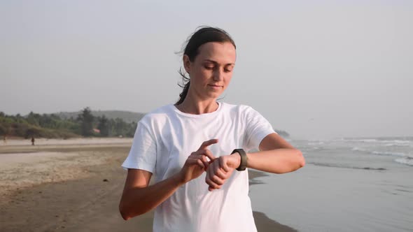 Woman is Jogging on the Ocean Beach and Using Fitness Watch Timer