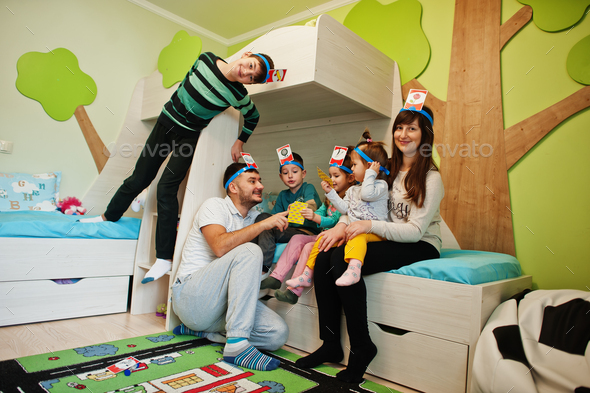 Happy family with four kids playing game guess who while having fun at home.