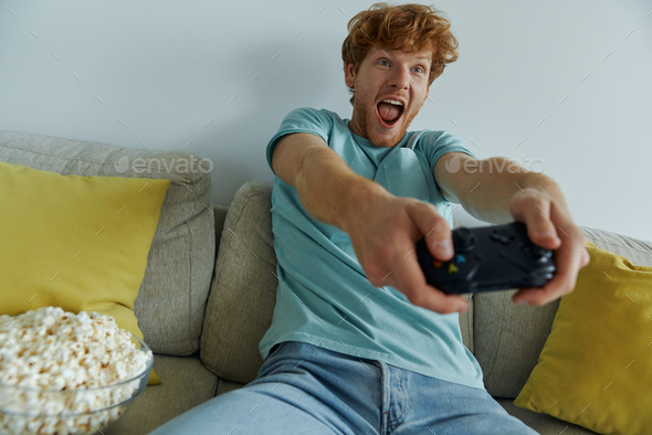 Excited young man using controller while playing video games on the couch at home