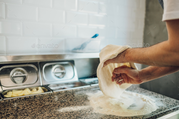 Kitchen chef preparing dough for pizza while working in a pizza place