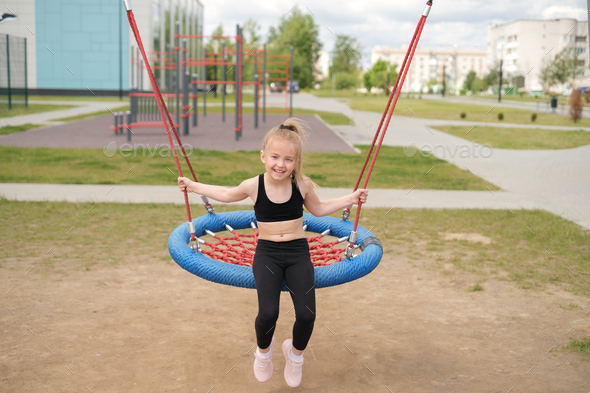 A girl swings on round swing on a playground Stock Photo by