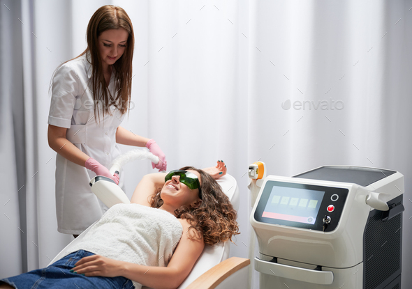 Woman receiving underarm laser hair removal treatment in beauty salon.