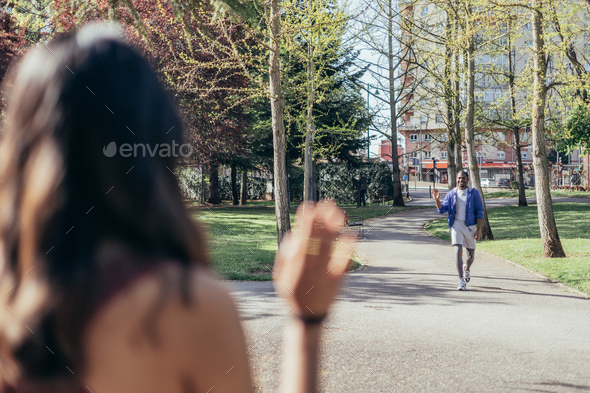 Just Friends. Girl Waving Hello Meeting Guy Walking In Park Outside. Selective Focus