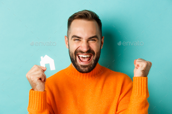 Real estate. Cheerful man buying apartment, rejoicing and saying yes, showing small paper house