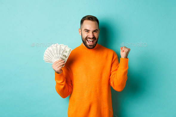 Shopping. Cheerful guy holding money, winning prize in cash and making fist pump, triumphing with