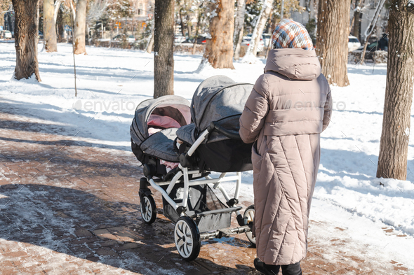 Grandmother pushing a baby stroller for twins walking outside in winter