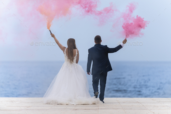Wedding couple with colored smoke flares and the sea and sky in the background