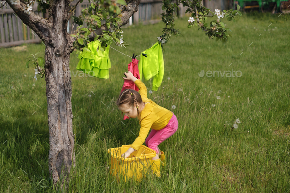 Girl hangs wet laundered clothes on clothesline under tree