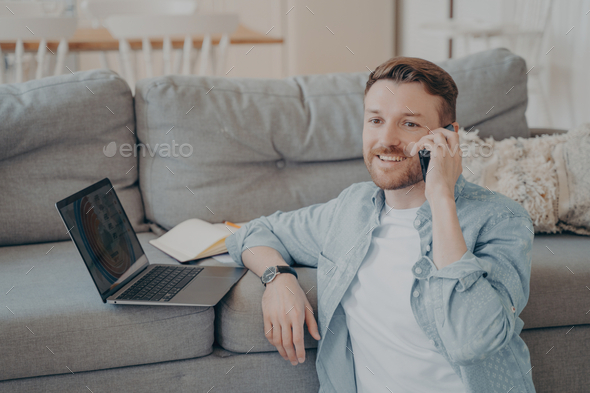 Young male company employee working remotely from home calling boss to tell good news