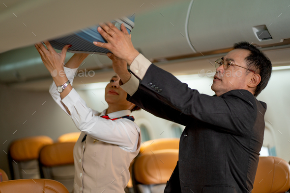 Business man bring his luggage to overhead shelf in airplane and air hostess help and support him