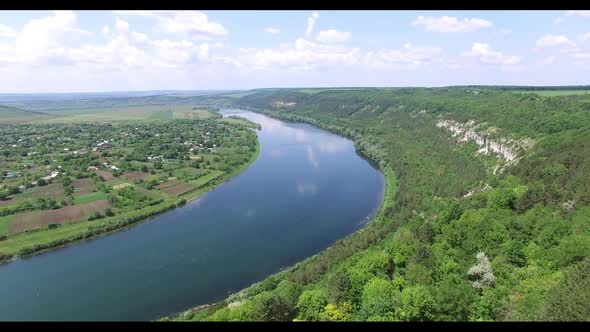 View of the countryside with houses, fields and trees which are surrounded by wide river alt