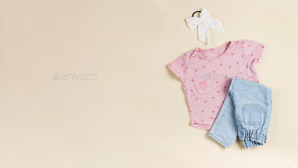 Children\'s pink T-shirt, folded jeans and elastic band for hair on a beige background. Copy space.