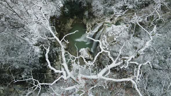 Waterfall Flowing Down From Rocks Shot Through the Branches of a Tree in Winter alt
