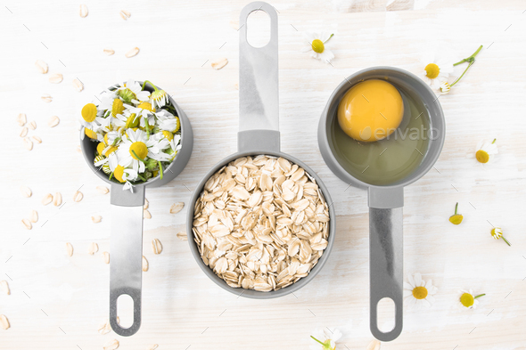 Natural ingredients for home cosmetics. Chamomile flowers, oatmeal and an egg in a container.