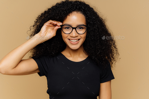 Woman grins at camera, keeps hand on rim of spectacles, glad to hear good news!