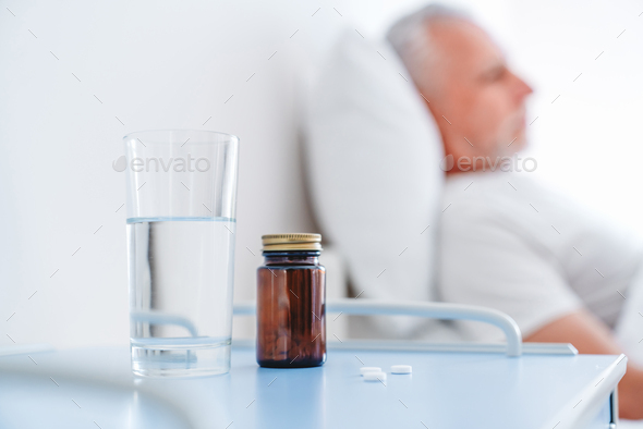 Medicine and healthcare concept. Old man sleeping in bed at hospital ward pills