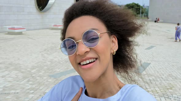 Fashionable Modern Joyful African American Curly Haired Girl with Blue Glasses Video Blogger Walks alt