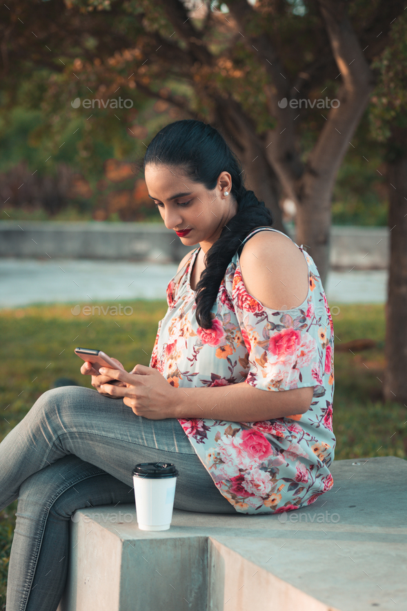 latin woman sitting in the park drinking ca - Stock Photo - Images