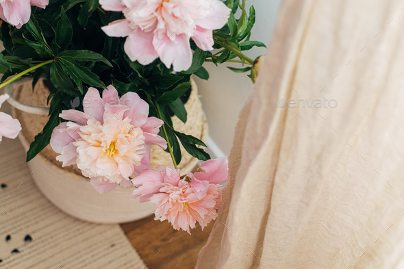 Beautiful peonies bouquet in basket at linen curtains in boho room. Modern bohemian decor, moody