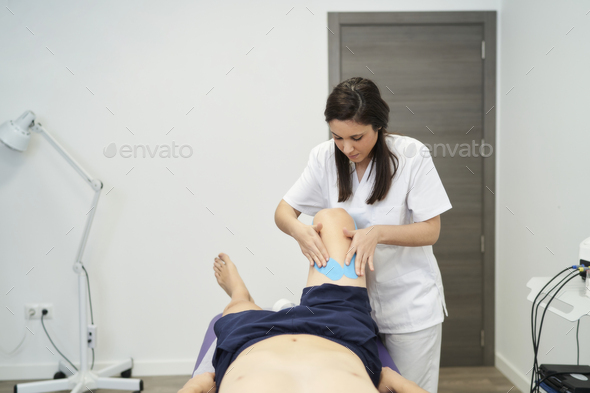 physiotherapist treating the patient\'s knee with neuromuscular taping