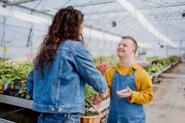Happy young employee with Down syndrome working in garden centre, taking payment from customer.